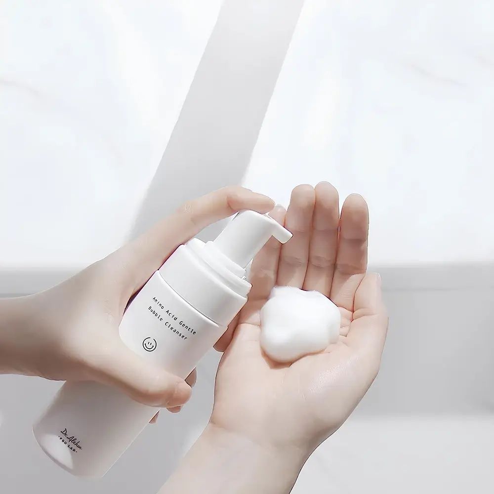 Mani che tengono un flacone bianco e schiuma. Scritta: Amino Acid Gentle Bubble Cleanser. Marchio: Dr. Althea.