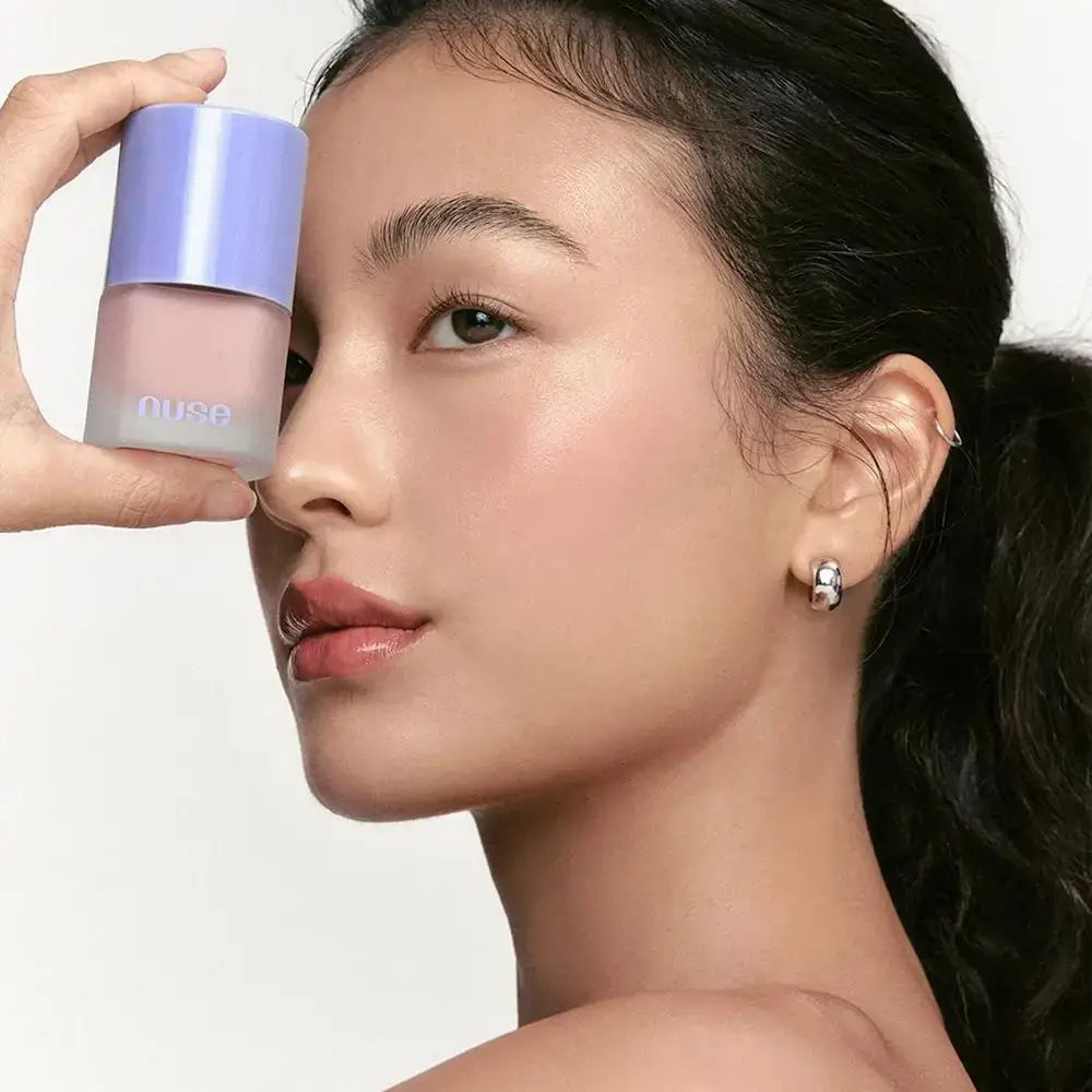 Donna che tiene in mano un flacone di NUSE Liquid Care Cheek 03 Pale Blossom. Prodotto davanti al viso.