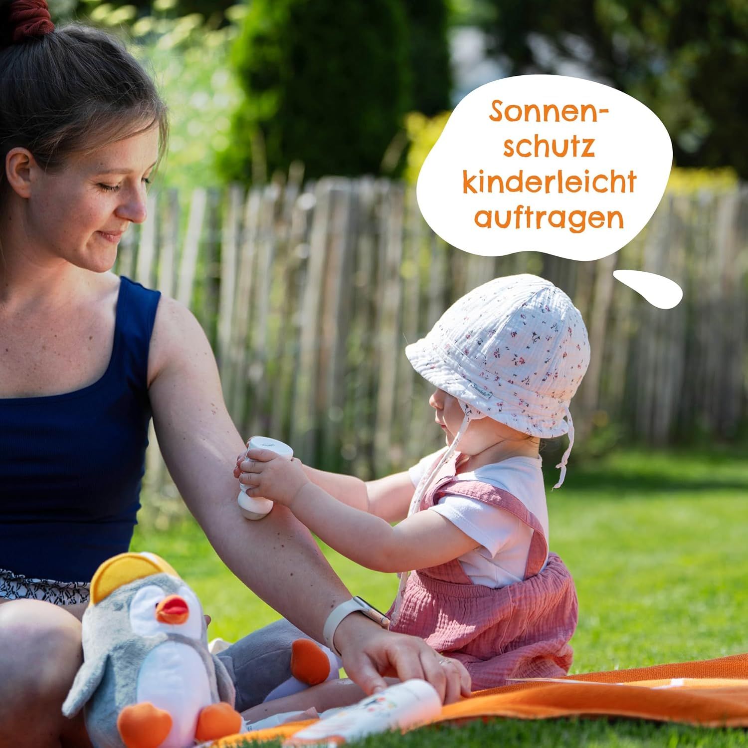 Madre applica roll-on solare sul braccio di un bambino. Seduti sull'erba. Fumetto: Applicare facilmente la protezione solare. Peluche pinguino.