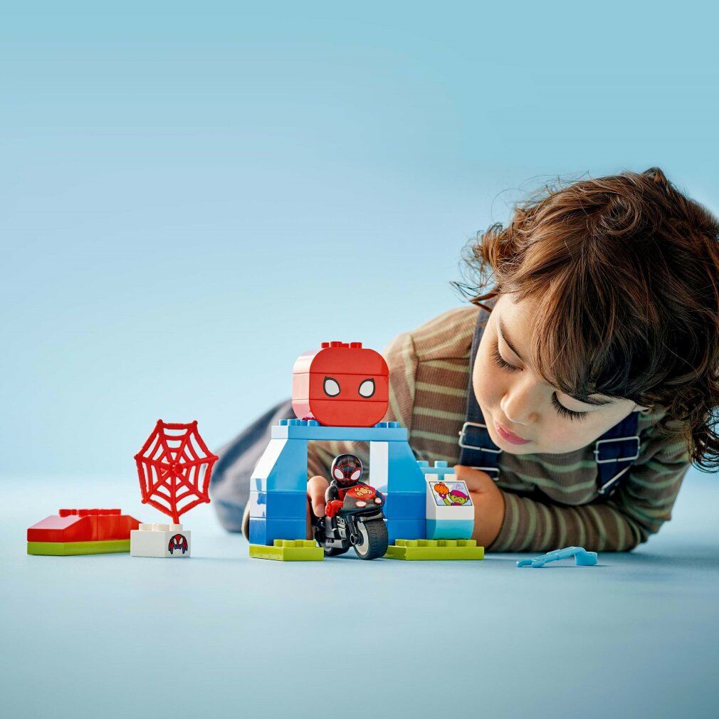 Bambino che gioca con il set LEGO Duplo. Moto, personaggio, edificio, ragnatela. Su sfondo blu.