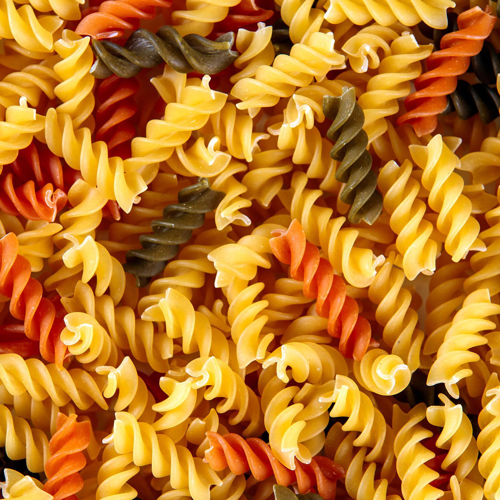 Primo piano di pasta fusilli tricolore. Vari colori: giallo, rosso, verde. Forma a spirale.