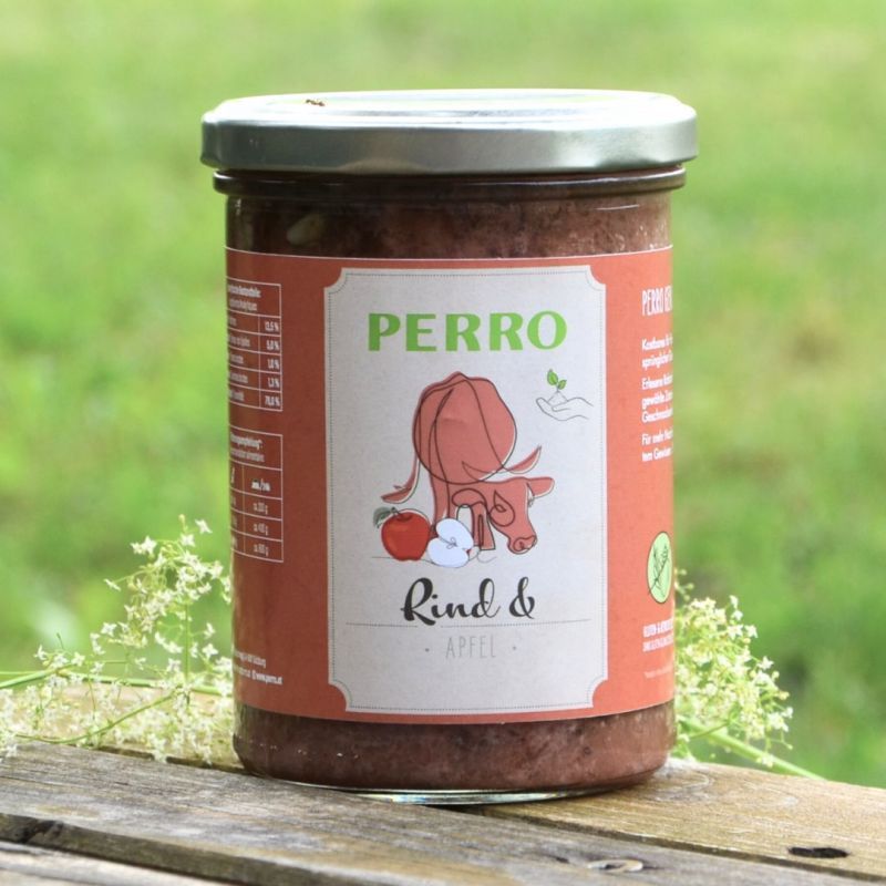 Vaso di vetro con etichetta rossa. Scritta PERRO, illustrazione di mucca e mela. Sfondo: erba verde.