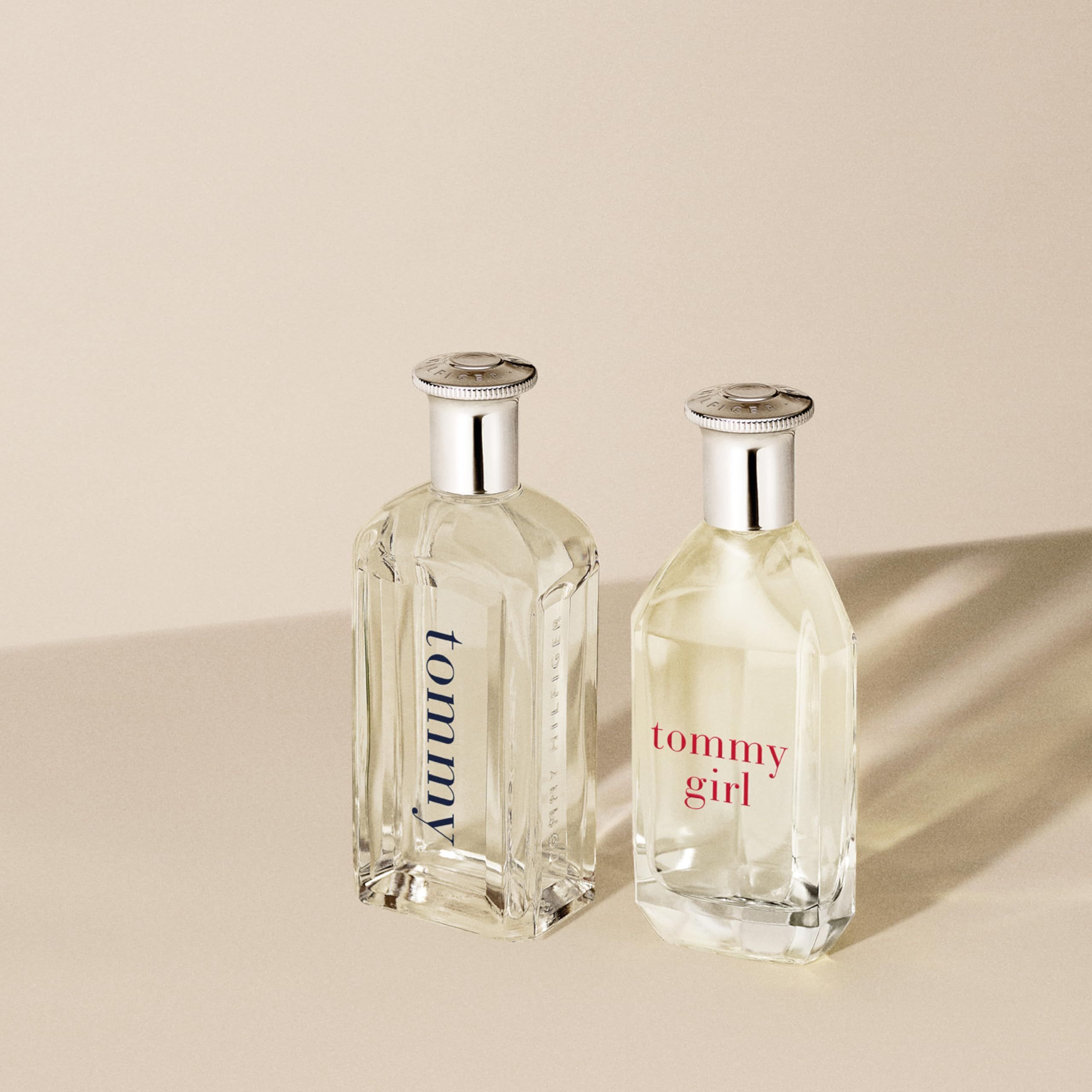 Due flaconi di profumo con tappi argentati. Uno con scritta "tommy girl". Flaconi rettangolari e trasparenti su sfondo beige.