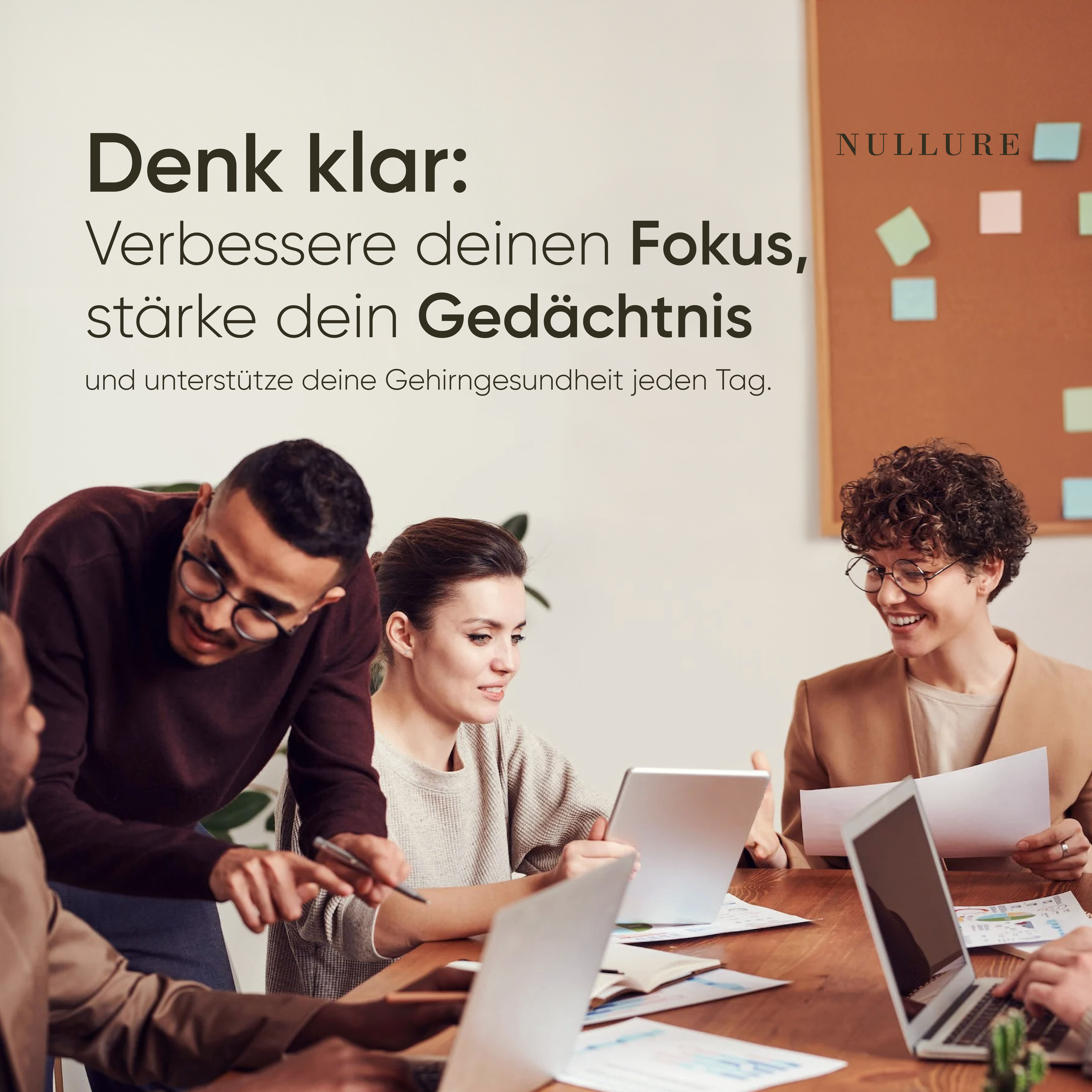 Ufficio con persone sedute a un tavolo. Laptop e appunti sul tavolo. Bacheca sullo sfondo.