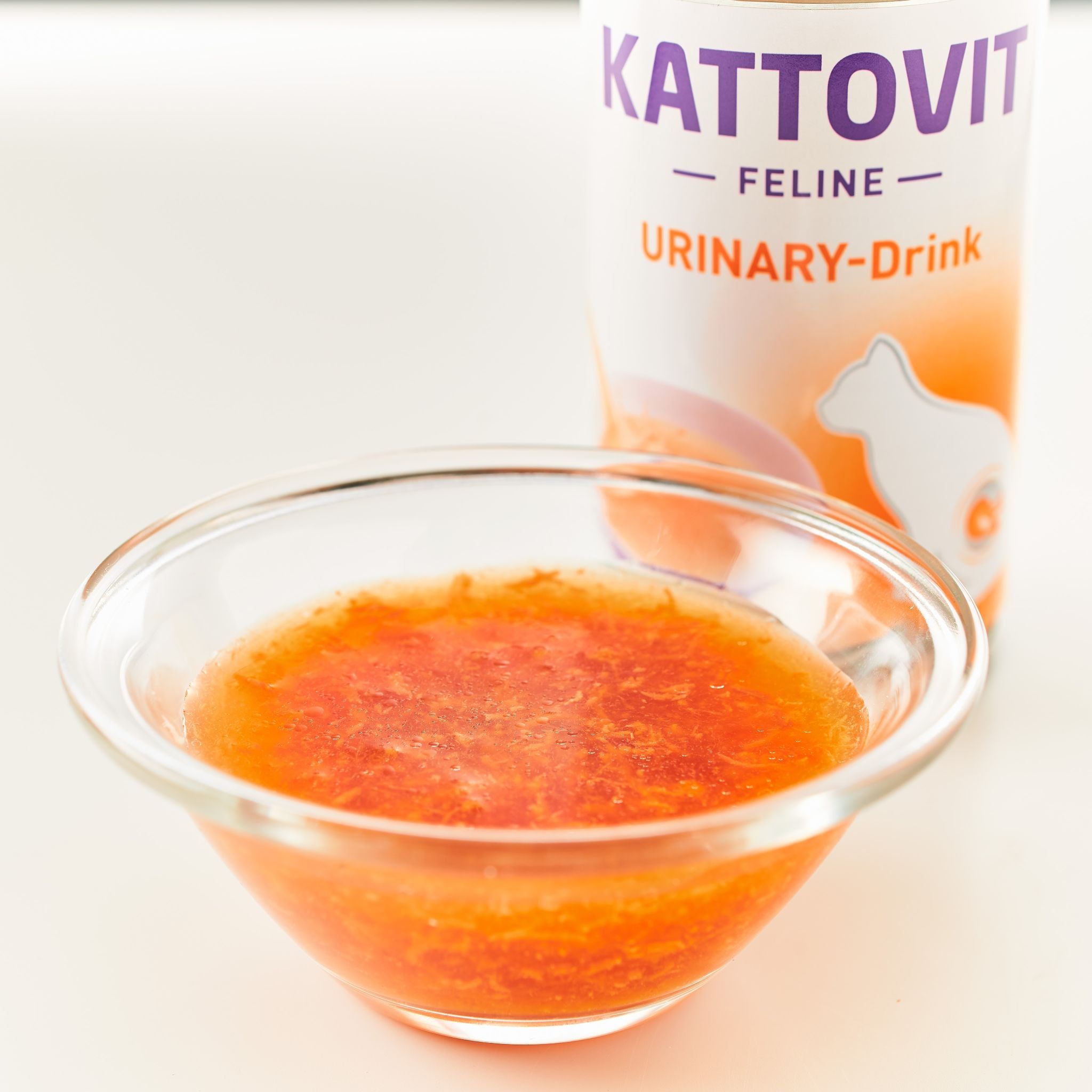Ciotola con liquido e lattina KATTOVIT Urinary-Drink. Liquido arancione. Lattina con etichetta bianca, testo arancione.