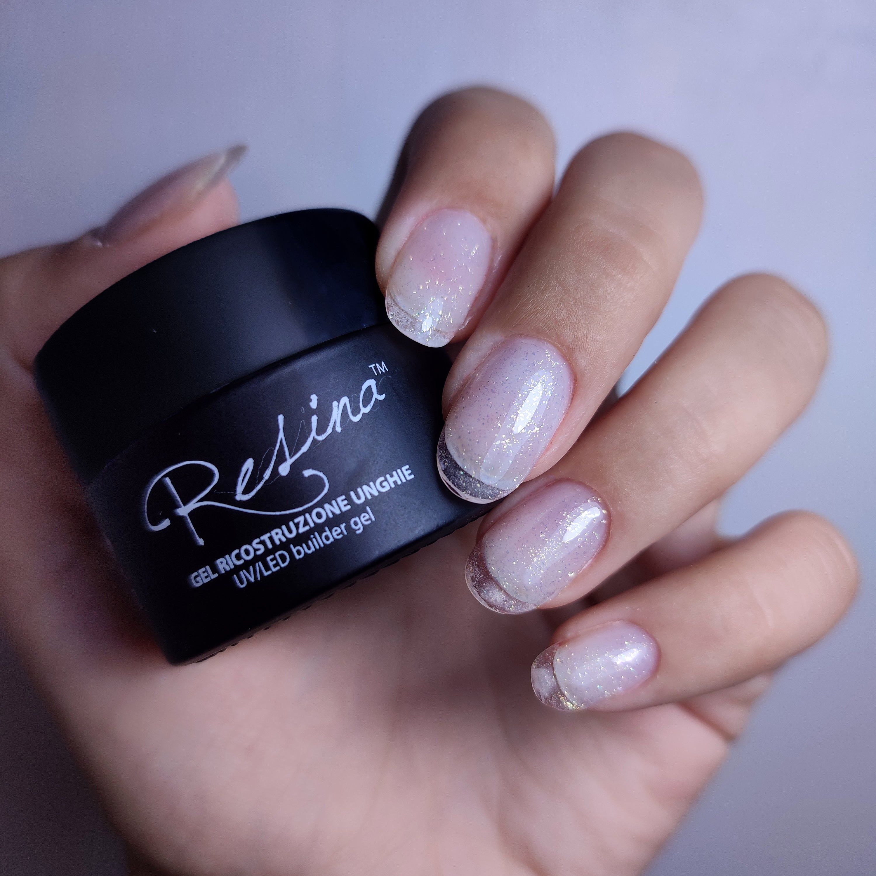 Mano con unghie smaltate e vasetto nero con scritta Resina. Gel ricostruzione unghie UV/LED.