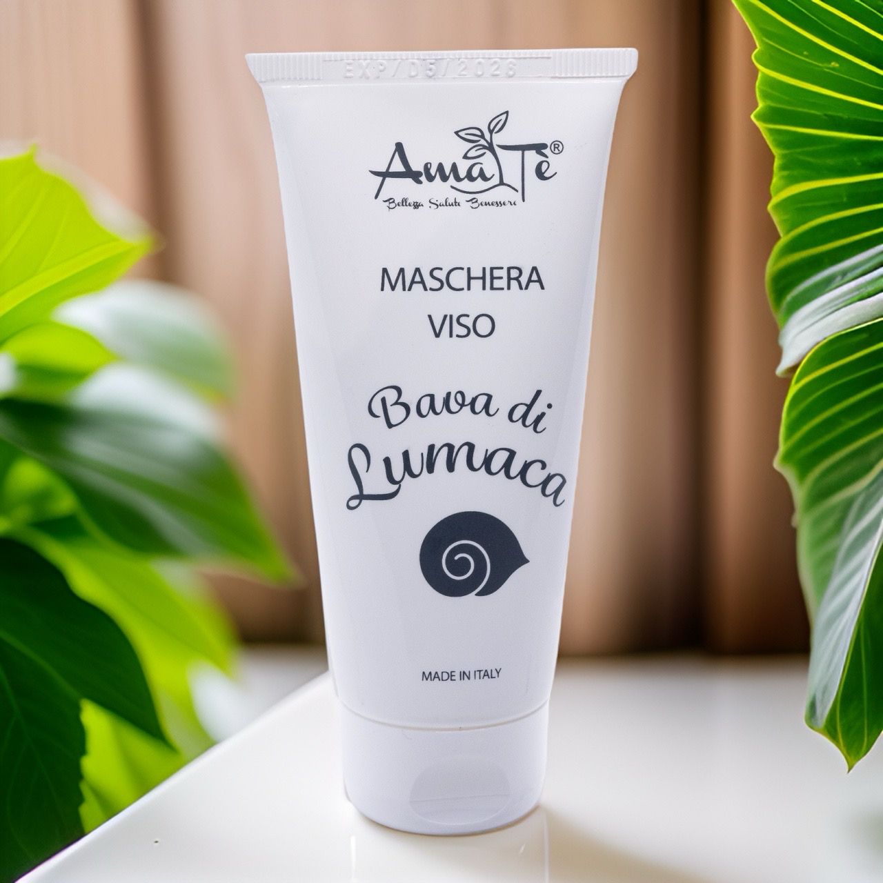 Tubo bianco con logo Amatè e testo: Maschera Viso Bava di Lumaca. Sfondo: legno e foglie.