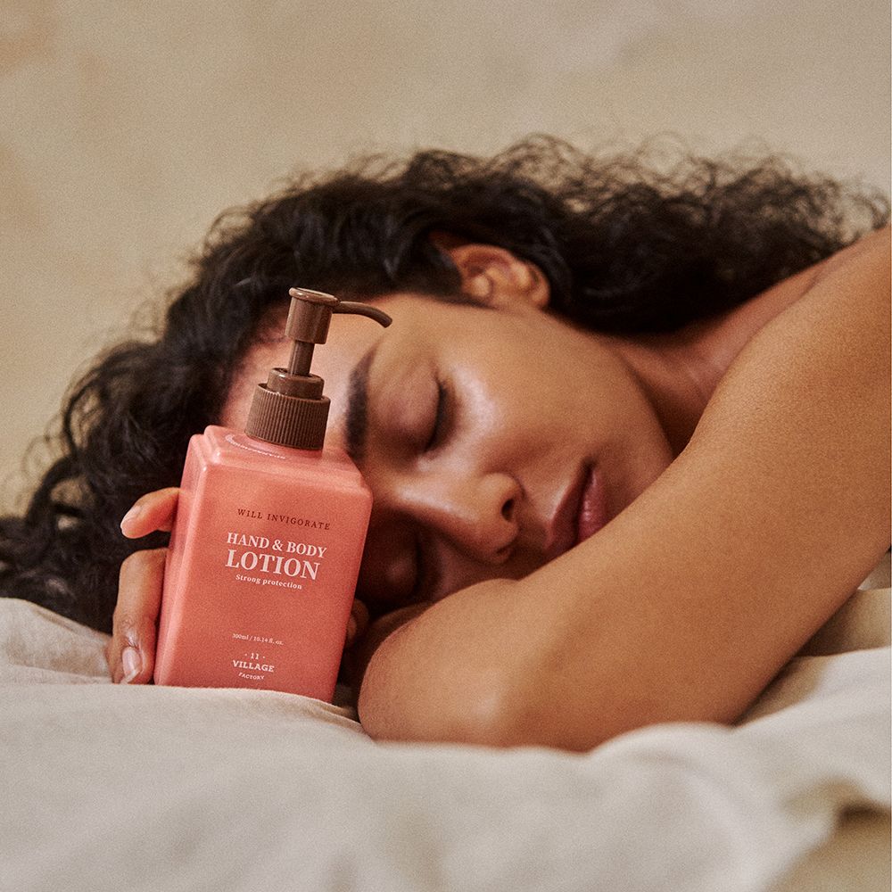 Lozione rosa per mani e corpo con dosatore a pompa. Appoggiata su un letto, accanto a una persona.