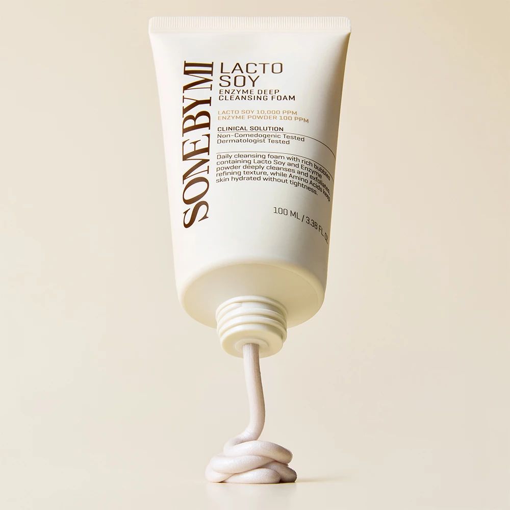 Un tubetto di schiuma detergente bianca, da cui esce un filo di prodotto. Sul tubetto c'è scritto "Lacto Soy Enzyme Deep Cleansing Foam".