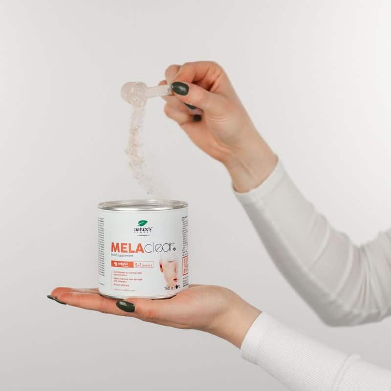 Mano versa polvere da cucchiaio nella lattina MELAclear+. Prodotto per un tono della pelle uniforme.