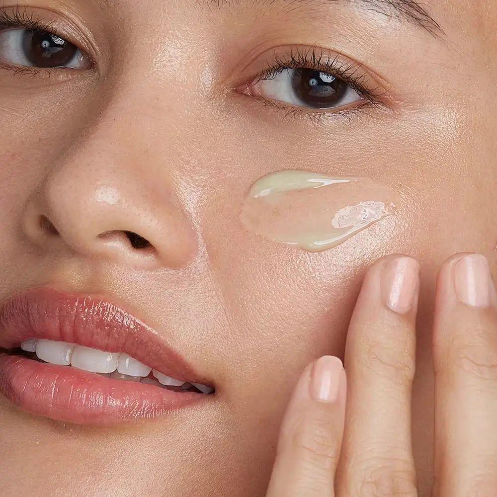 Viso di una persona con crema applicata. La crema è verde chiaro e viene applicata con un dito.