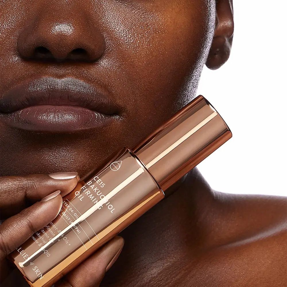 Flacone di olio color rame con nome e marchio del prodotto. Parzialmente visibile: volto di una persona.