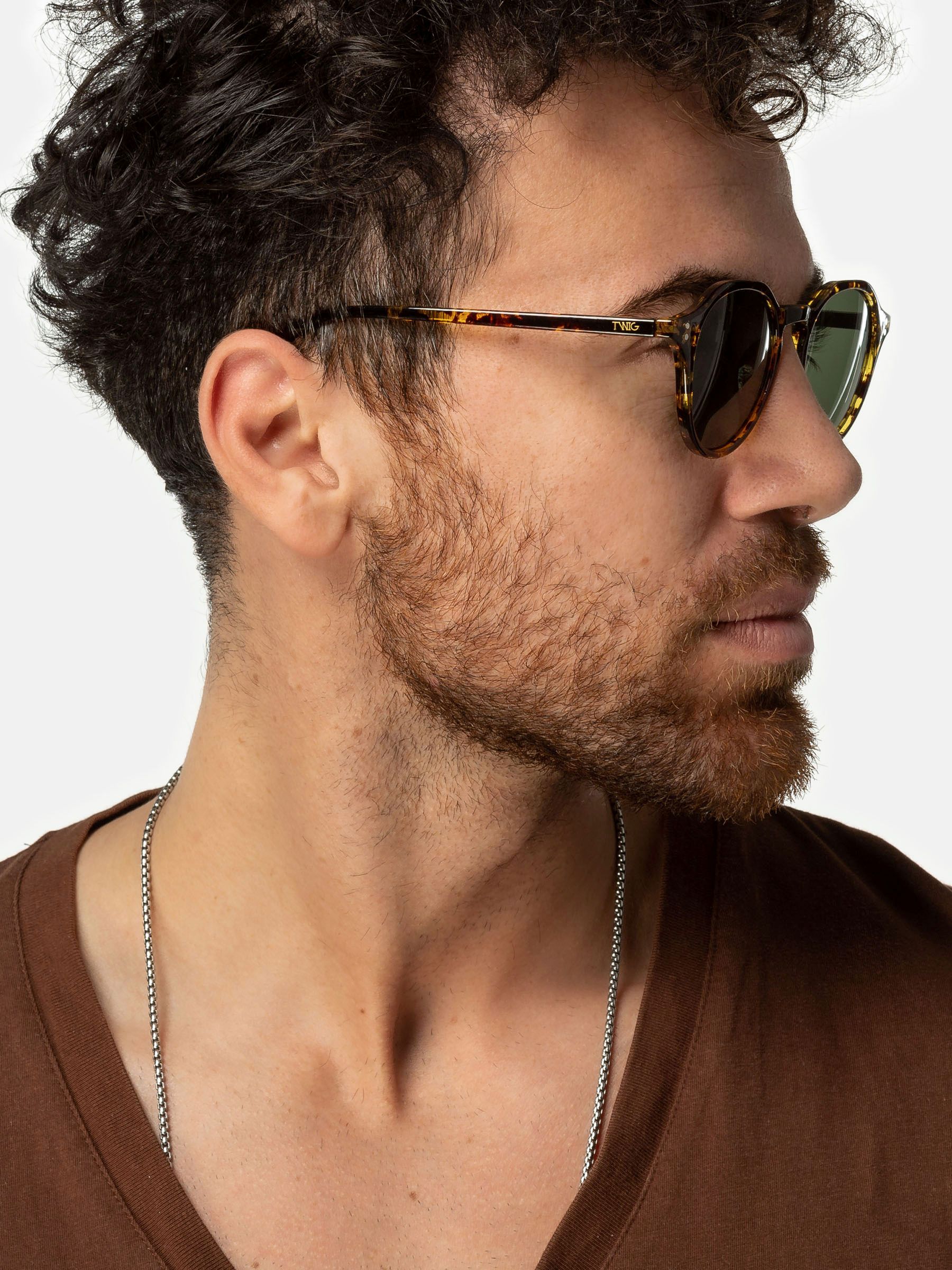 Uomo con occhiali da sole. Occhiali rotondi, motivo tartarugato marrone, lenti verdi. Vista laterale.