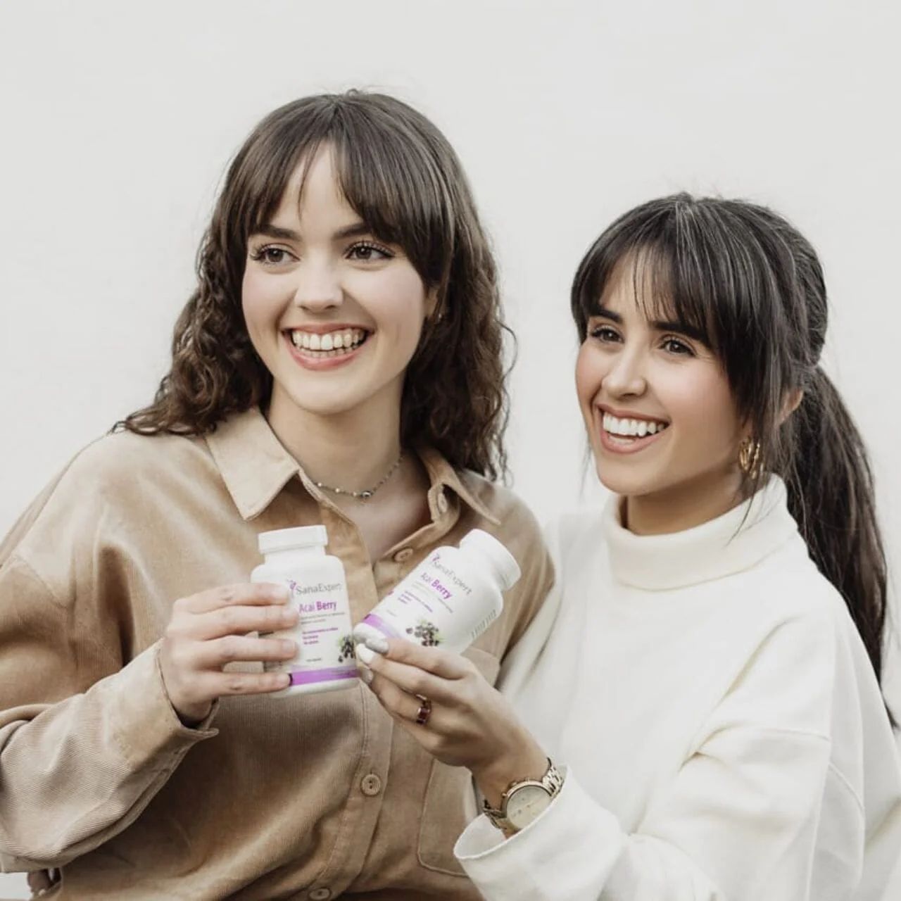 Due donne tengono bottiglie di SanaExpert Acai Berry. Il nome del prodotto e il logo sono visibili sulle bottiglie.