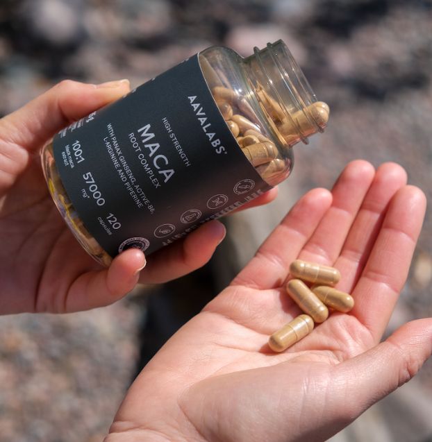Mano che tiene un flacone di capsule di Maca, alcune capsule nel palmo.
