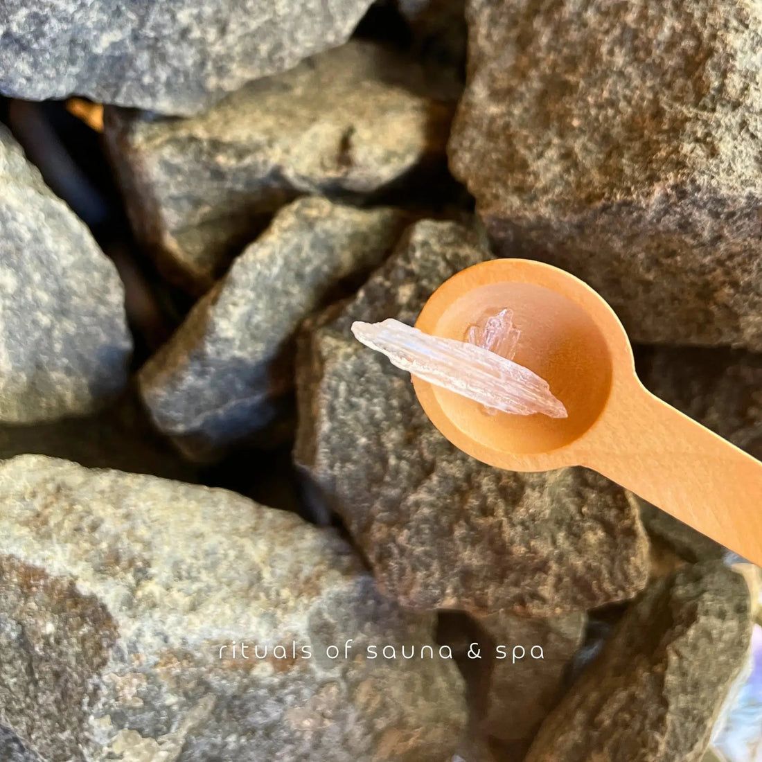 Cucchiaio di legno con cristallo di mentolo su pietre della sauna. Scritta: rituals of sauna & spa.