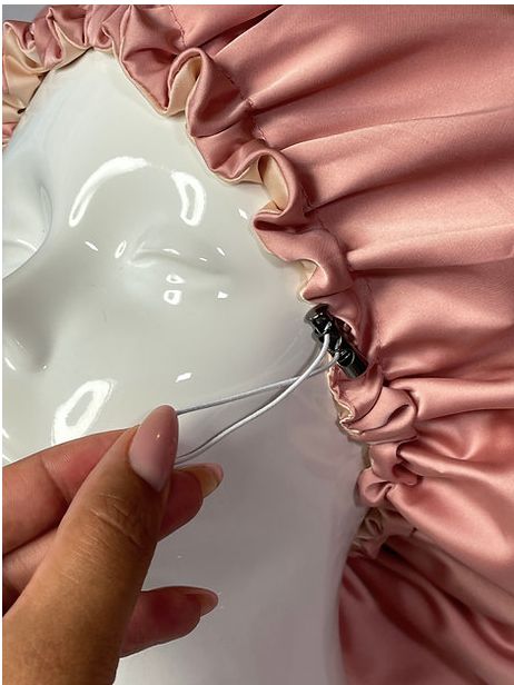 Primo piano di una mano che tira una cuffia in seta rosa. Cordino visibile.
