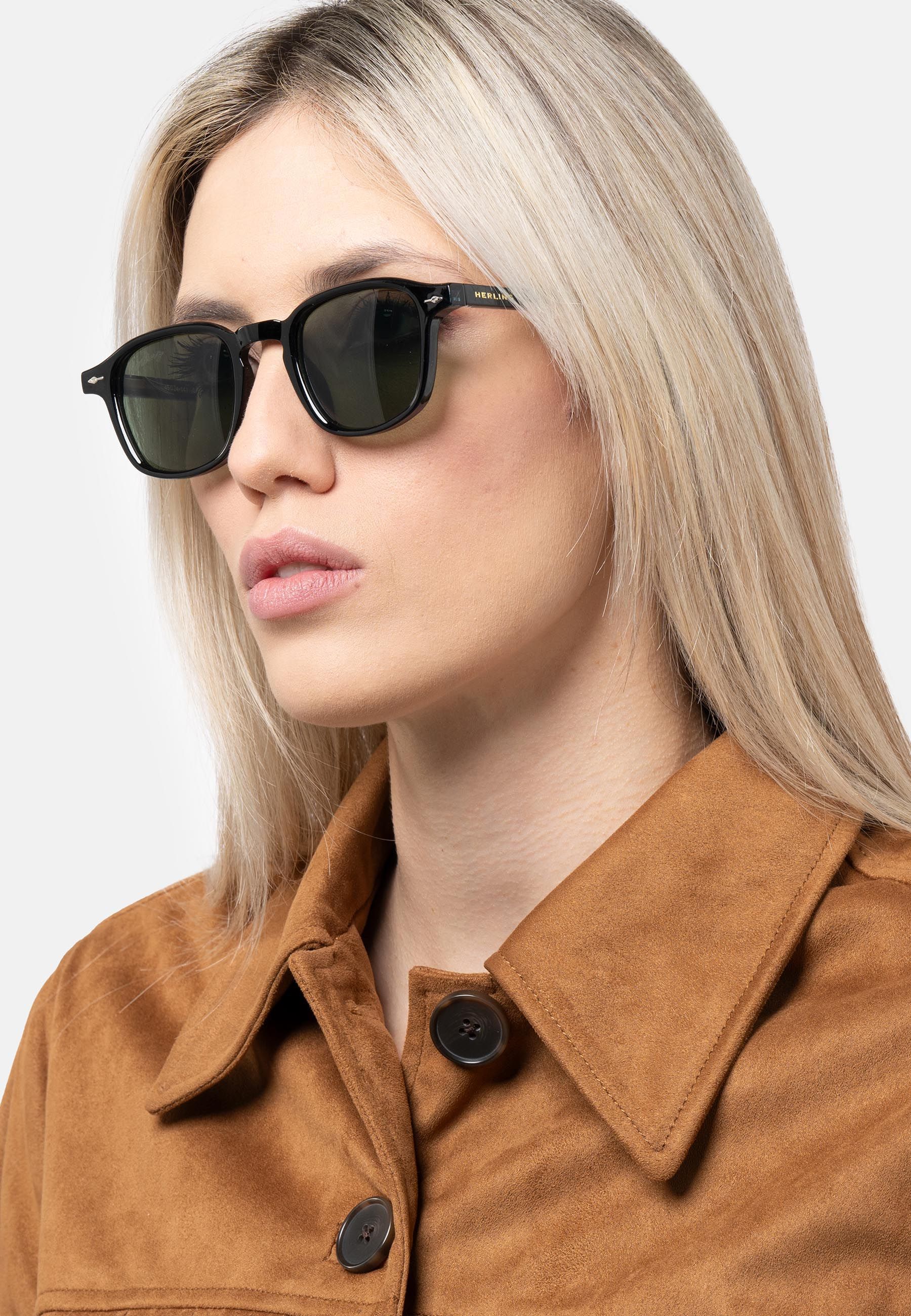 Donna con occhiali da sole neri con lenti verdi. Logo Herling sull'asta. Forma angolare.