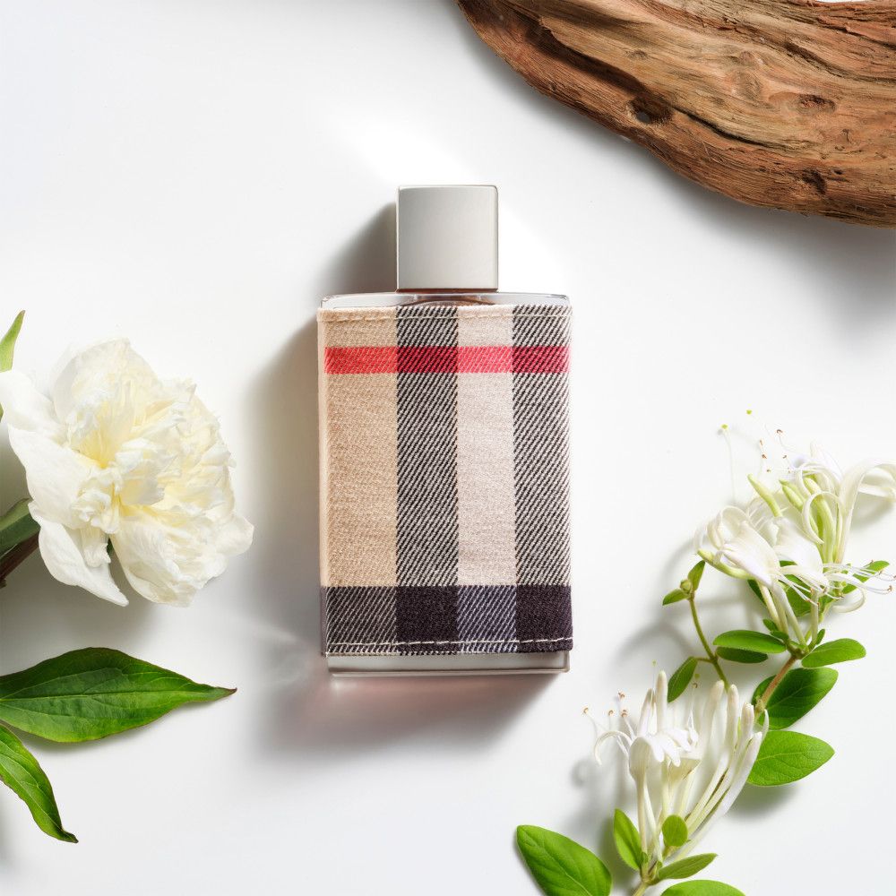 Flacone di profumo con rivestimento in tessuto a quadri. Fiori e pezzo di legno su sfondo bianco.