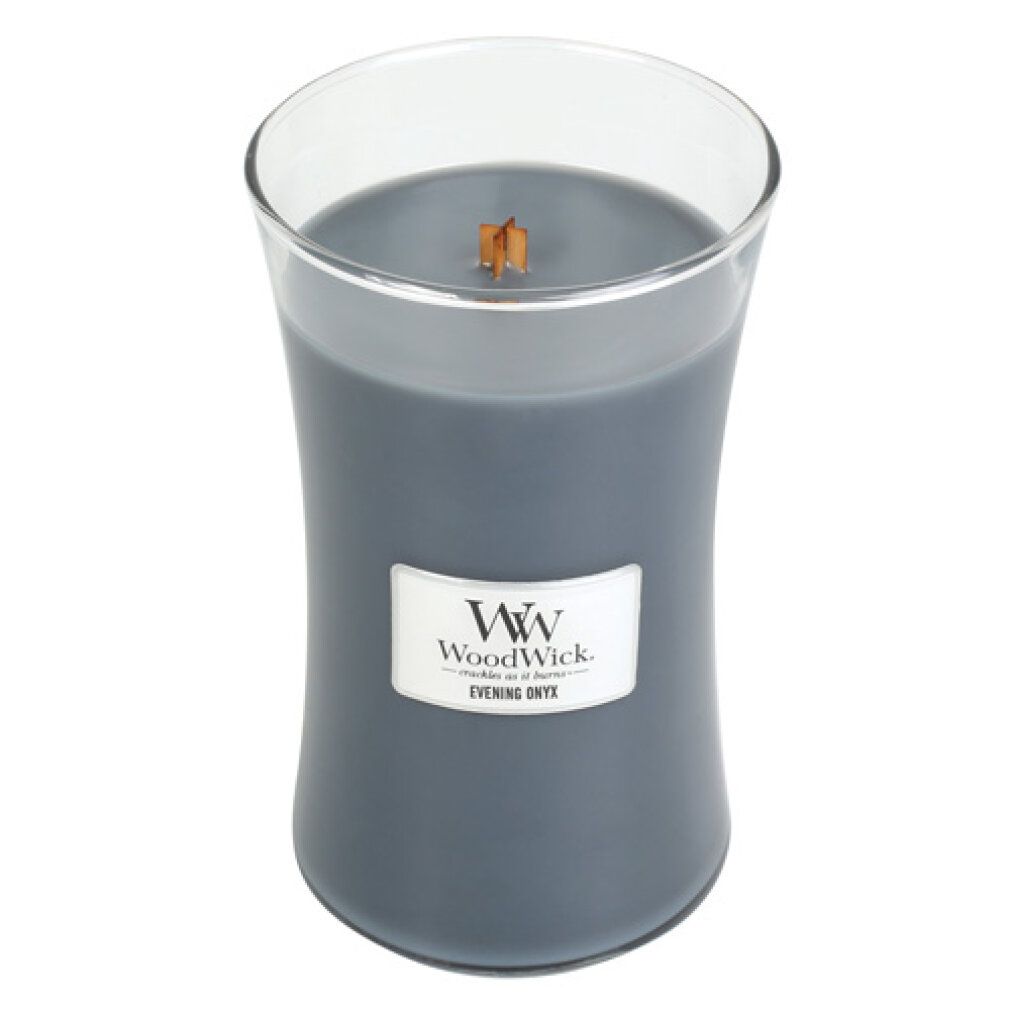 Candela grigia in vetro, senza coperchio. Etichetta "WoodWick Evening Onyx". Stoppino in legno visibile.