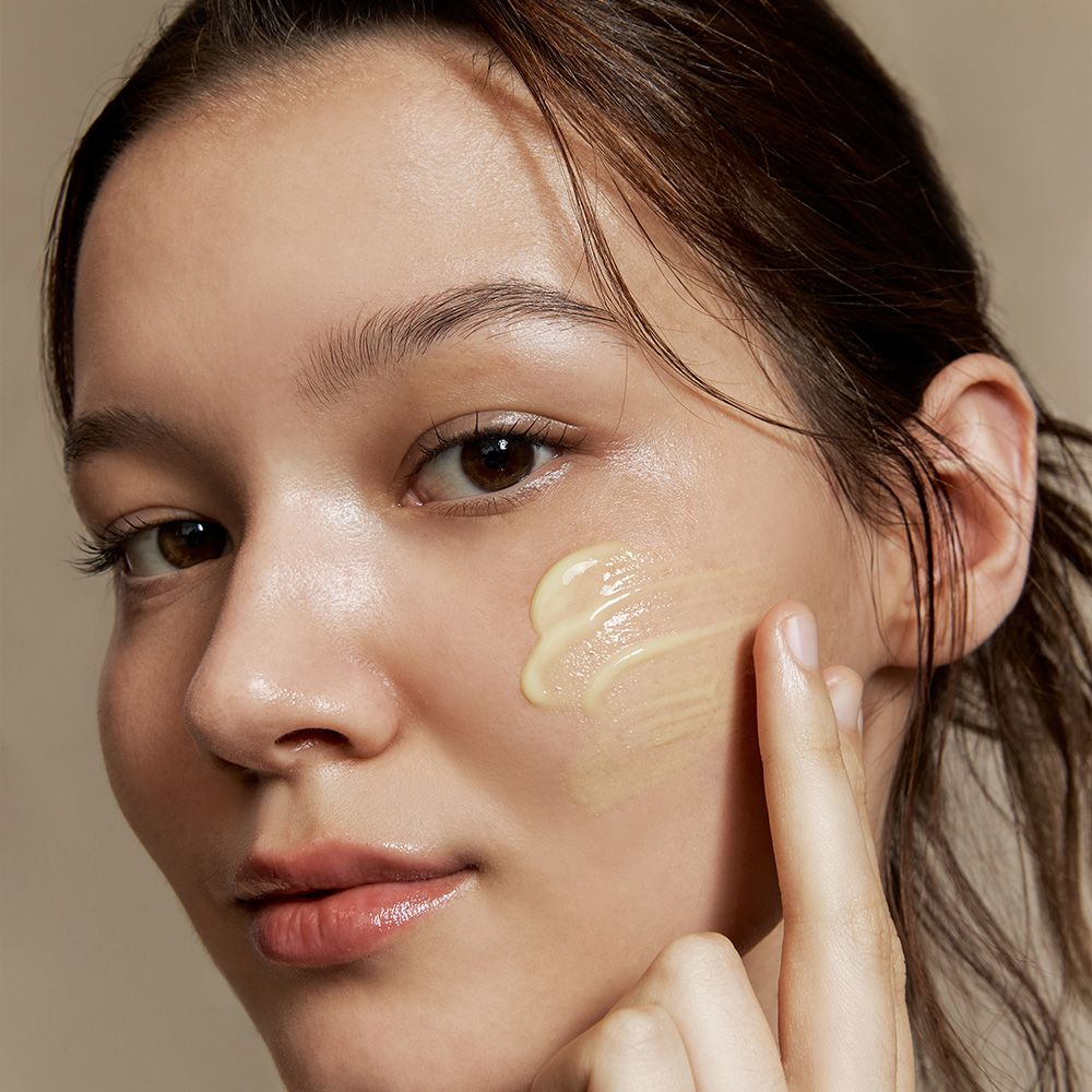 Una donna applica una crema gialla sulla guancia.