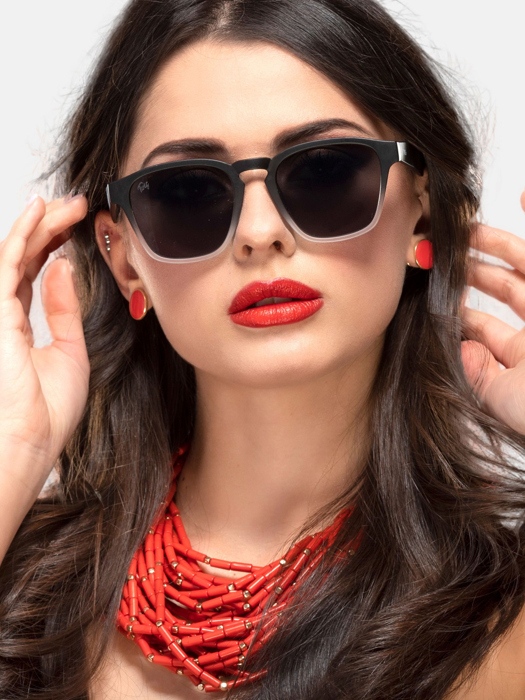 Donna con occhiali da sole neri con sfumatura grigia. Orecchini e collana rossi.