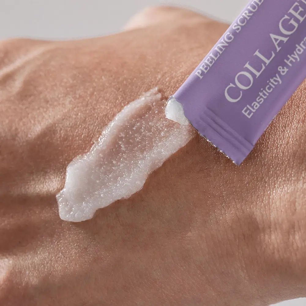 Peeling sulla mano. Bustina singola viola. Testo: Collagen Milky, Peeling Scrub, Elasticità & Idratazione.