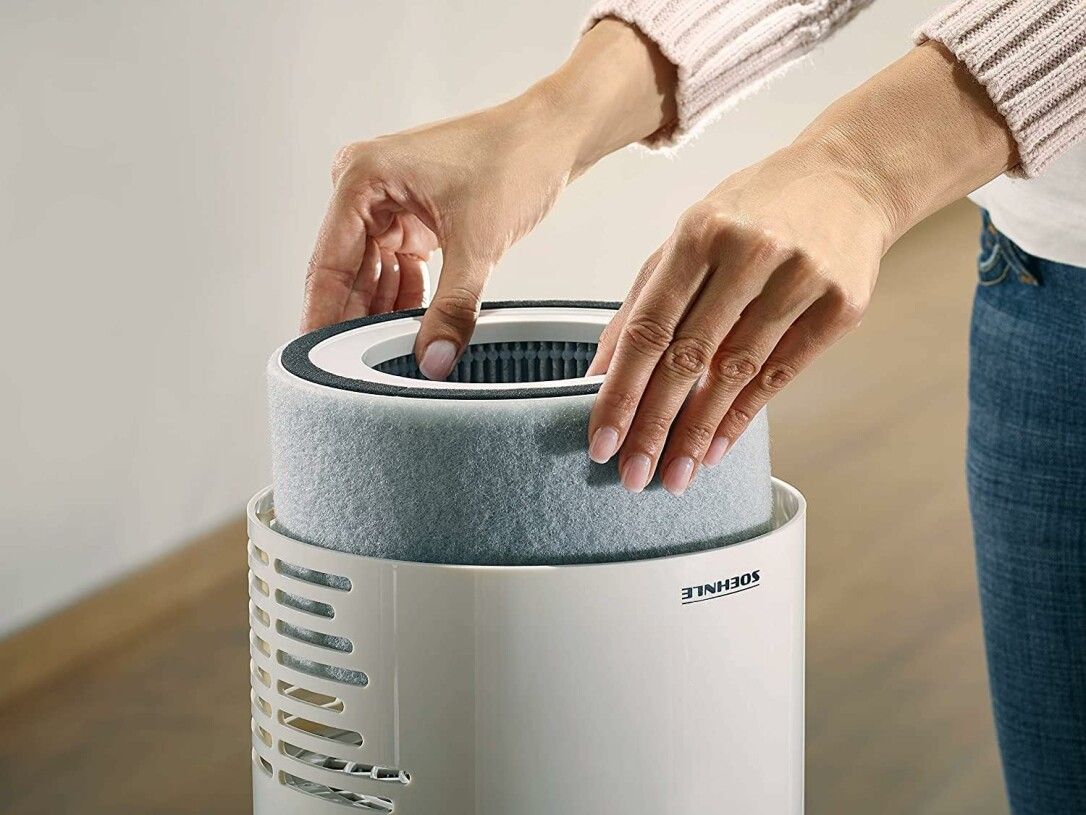Mani che inseriscono filtro grigio cilindrico in purificatore d'aria bianco. Logo Soehnle visibile.