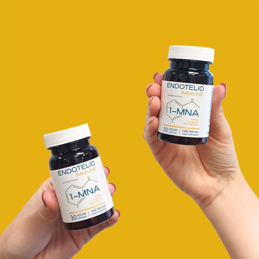 Due flaconi di capsule marroni in mano. Nome del prodotto e ingredienti sui flaconi. Sfondo giallo.