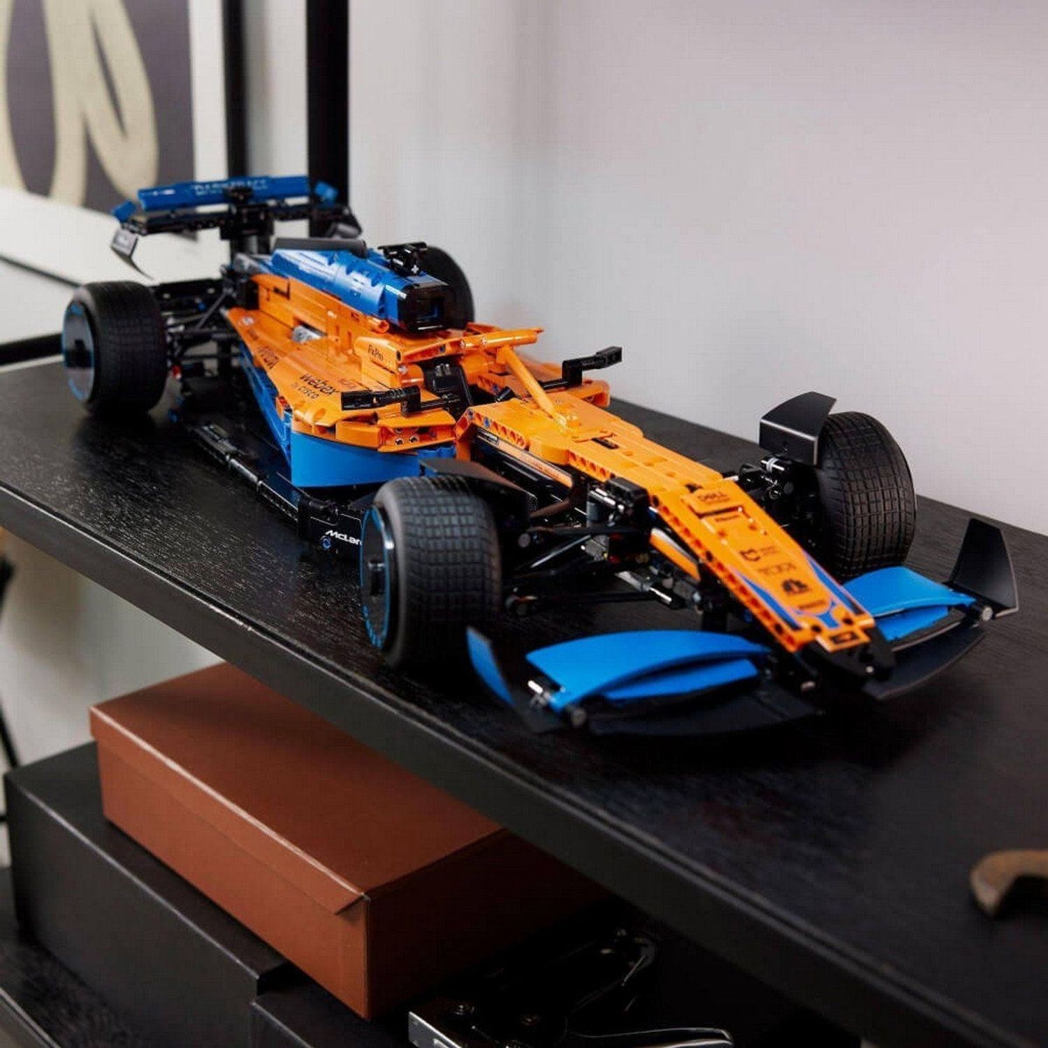 Auto di Formula 1 arancione e blu fatta con mattoncini LEGO su una mensola. L'auto ha pneumatici neri e il logo McLaren.