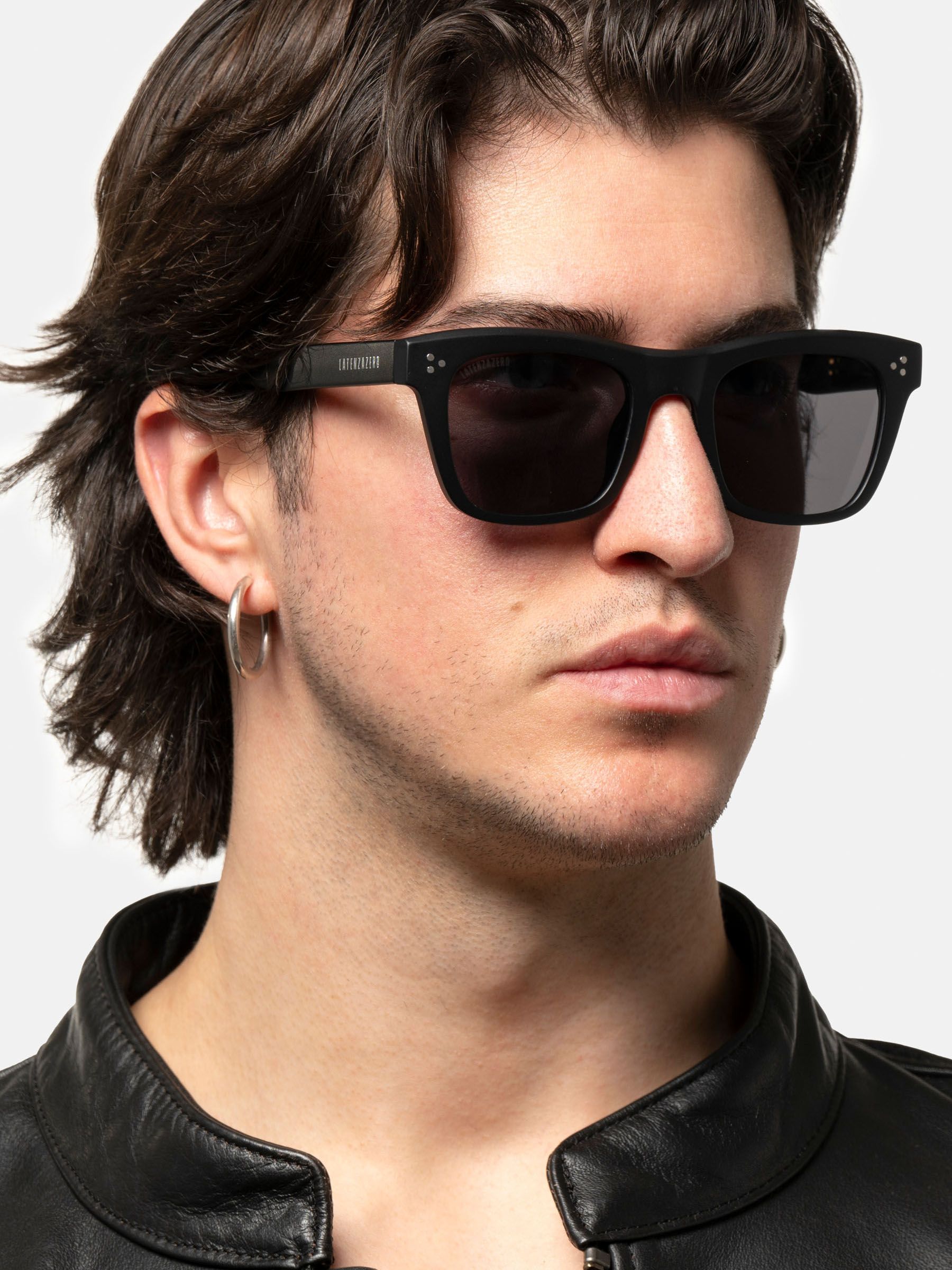 Uomo con occhiali da sole neri. "LATENZAZERO" sull'asta. Lenti quadrate. Montatura nera.