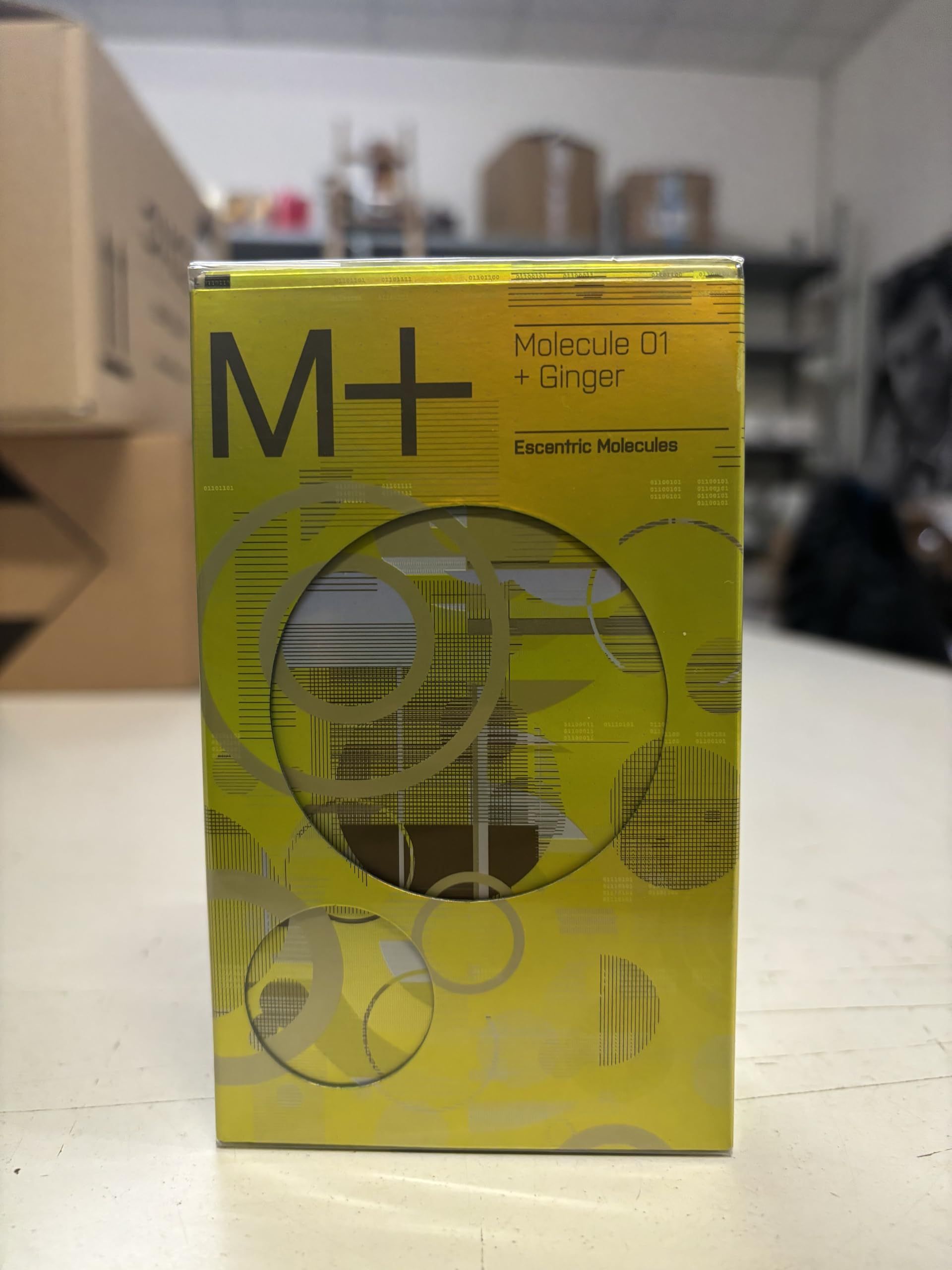 Scatola rettangolare gialla con cerchi argentati. Scritta: M+ e Molecule 01 + Ginger. Escentric Molecules.