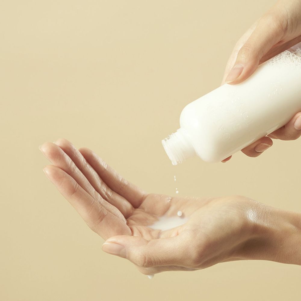 Mani che tengono un flacone bianco. Liquido versato nel palmo. Il liquido è bianco.