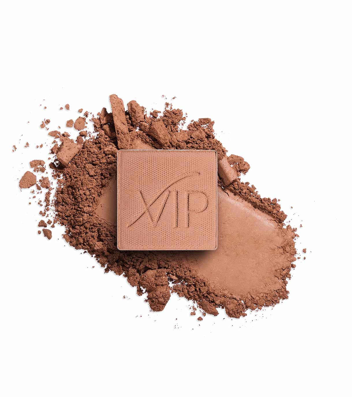 Bronzer compatto con logo in rilievo, circondato da cipria sciolta marrone.