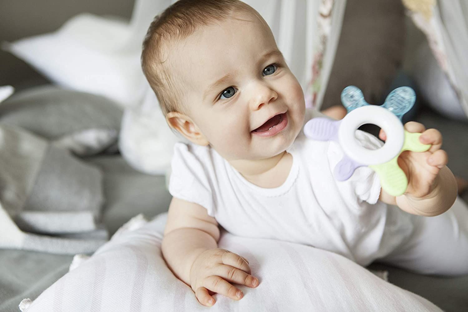 Bambino tiene anello refrigerante. Bambino sorridente su cuscino. Anello blu, verde, viola e bianco.