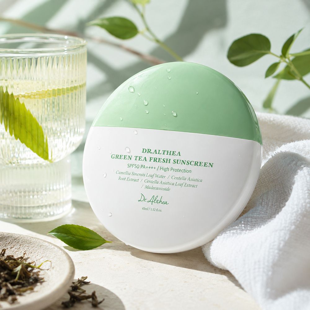 Protezione solare Dr. Althea in confezione bianca e verde, accanto a un bicchiere d'acqua e tè verde.