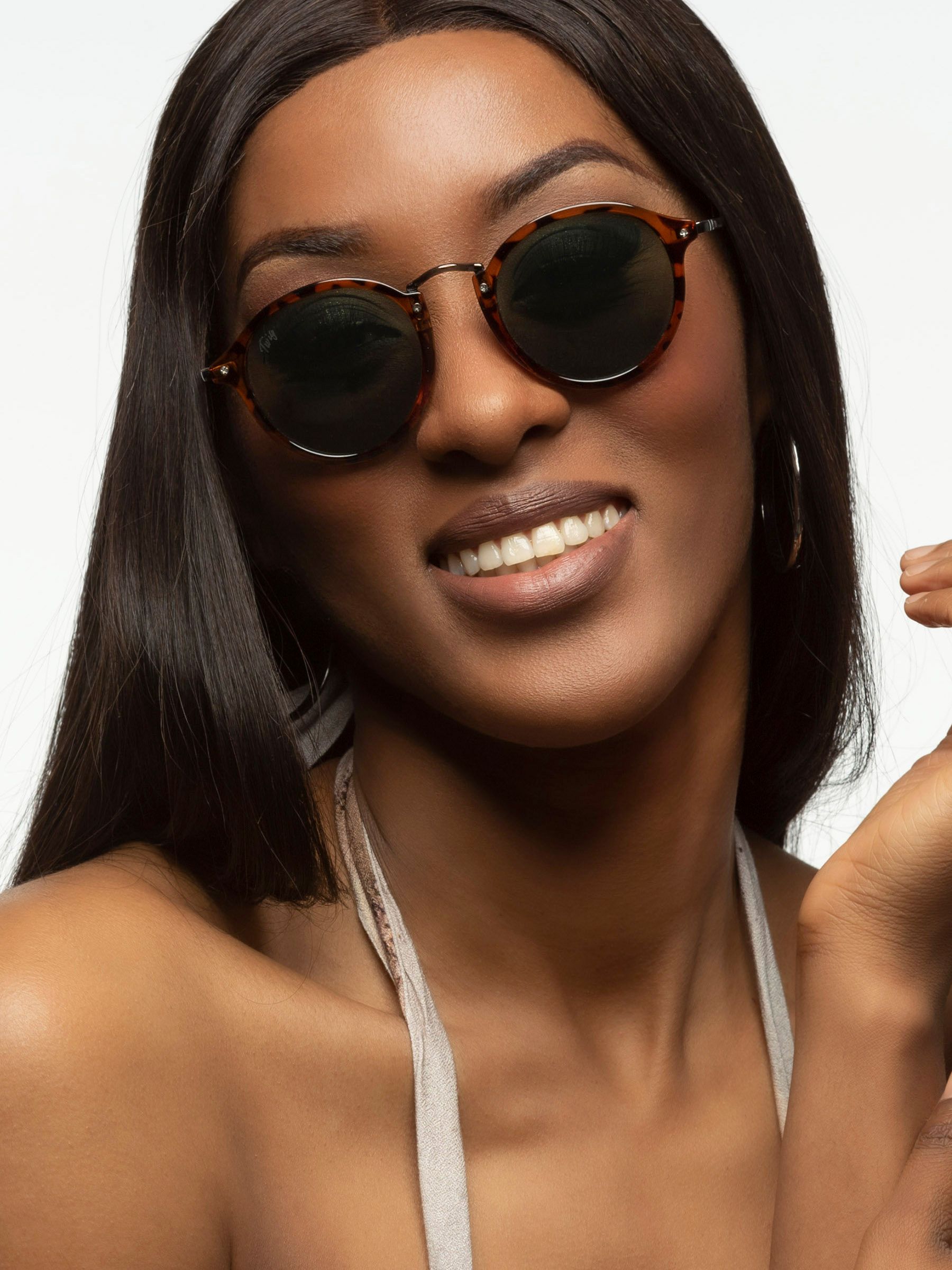 Donna con occhiali da sole Twig. Forma rotonda, montatura marrone tartarugato, lenti verdi. Logo Twig.