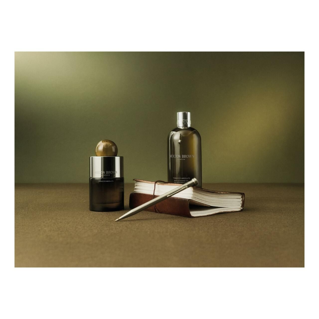 Flacone e flacone marrone scuro accanto a taccuino e penna. Marchio Molton Brown visibile.