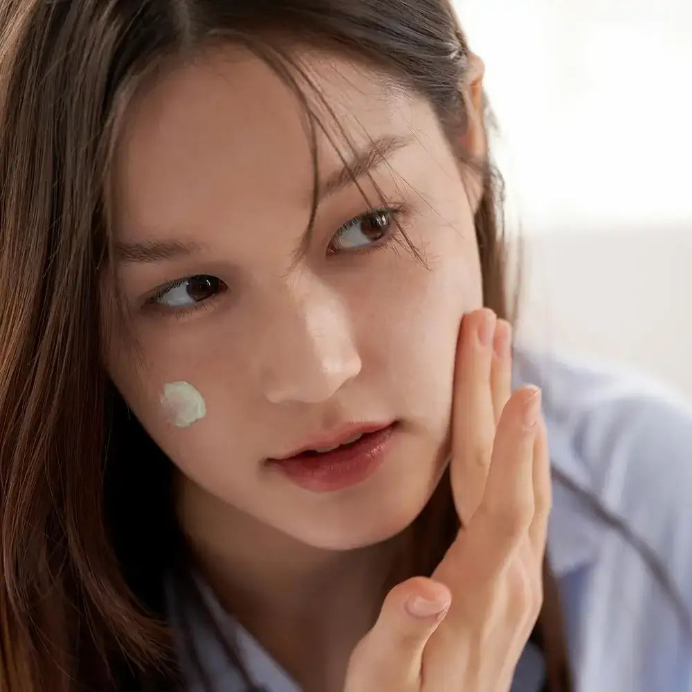 Donna applica trucco. Sulla pelle una goccia di primer verde. Tocca il suo viso.