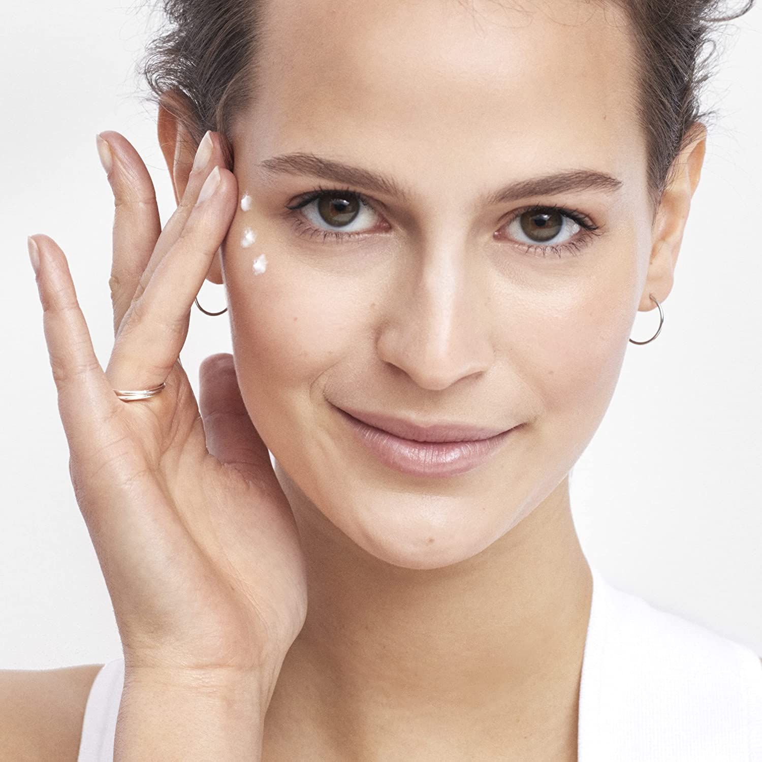 Donna applica crema. Pelle chiara, abiti chiari. Punti di crema sotto gli occhi.
