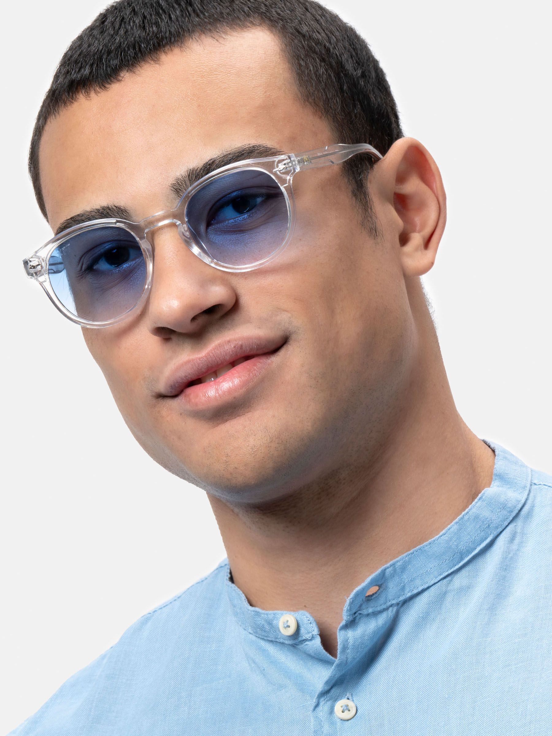 Uomo con occhiali da sole con montatura trasparente e lenti blu. Primo piano, camicia azzurra.