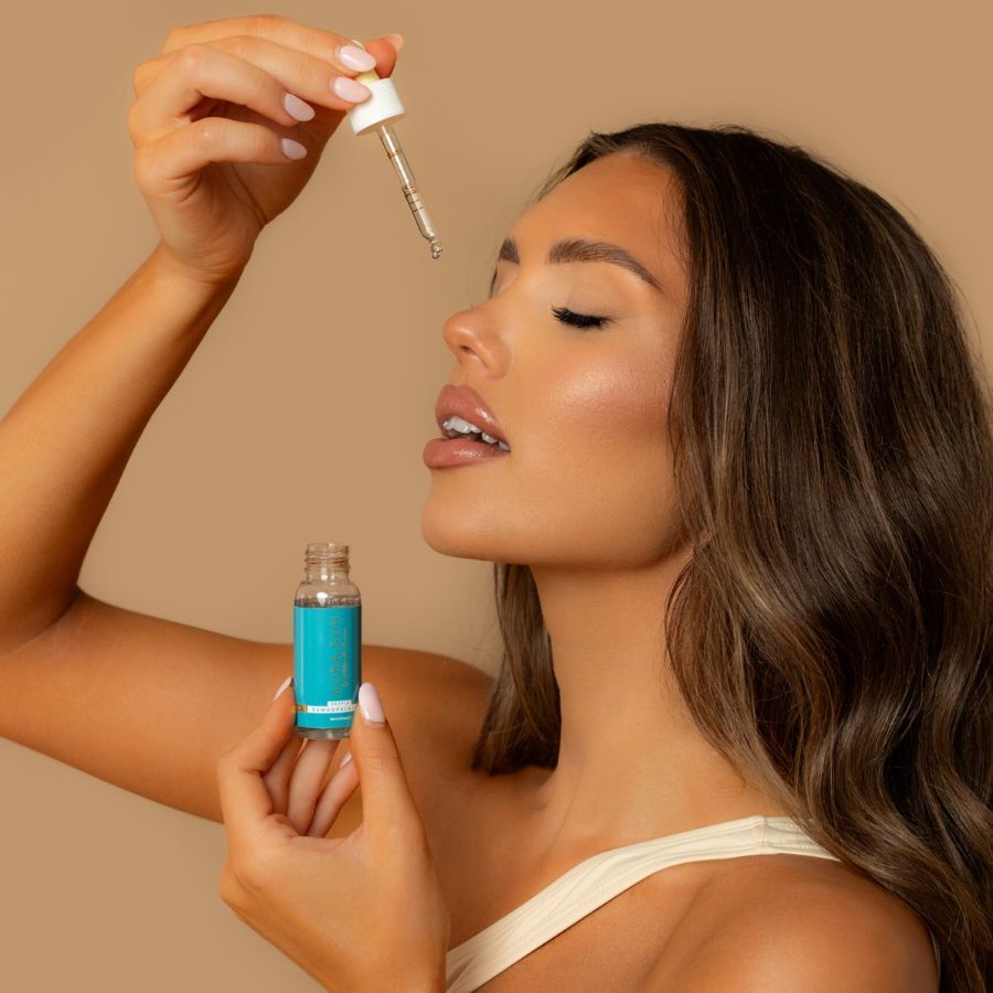 Una donna tiene una piccola bottiglia di vetro con etichetta blu e un contagocce con siero sopra il viso.