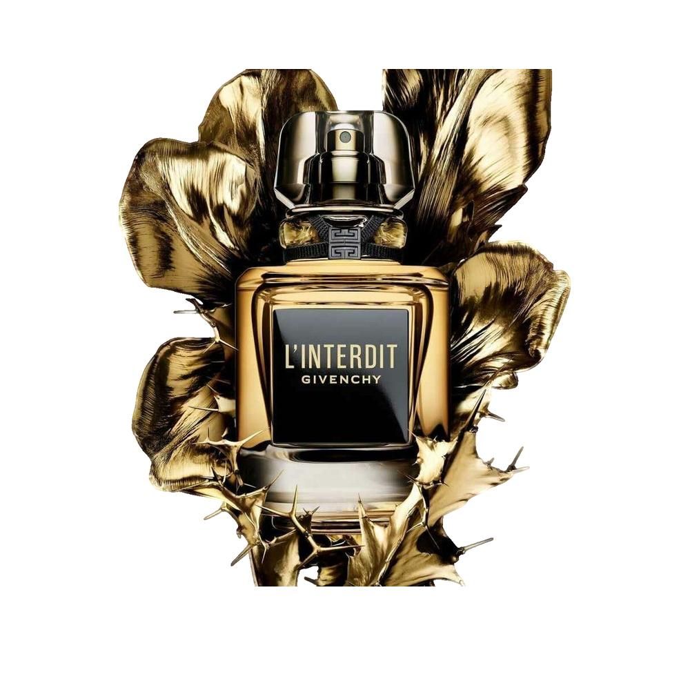 Flacone di profumo con etichetta nera e liquido dorato. Scritta L'INTERDIT e GIVENCHY. Circondato da foglie dorate.