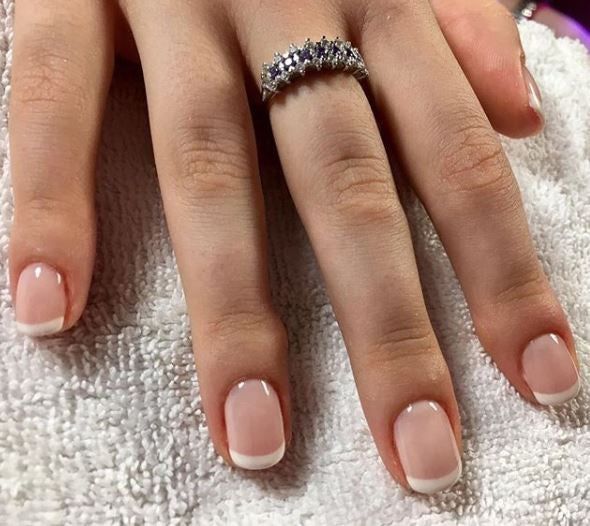 Primo piano di unghie con french manicure. Unghie chiare con punta bianca. Mano con anello su asciugamano bianco.