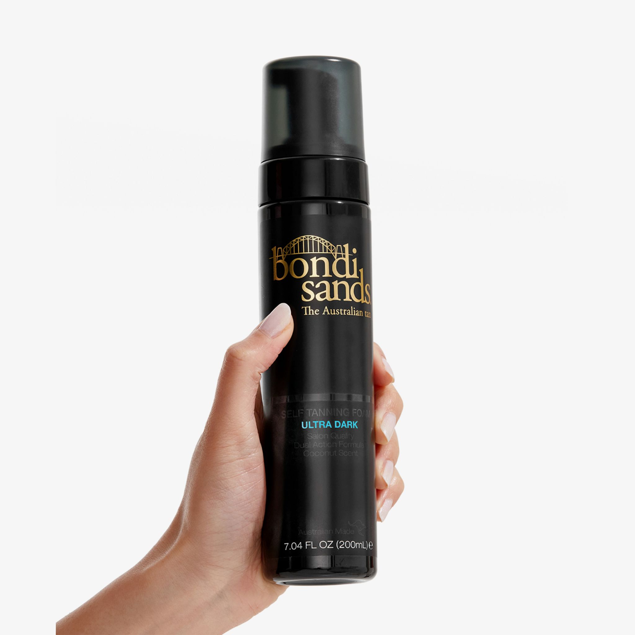 Mano che tiene un flacone nero con erogatore nero. Scritta: Bondi Sands, schiuma autoabbronzante Ultra Dark. 200ml.