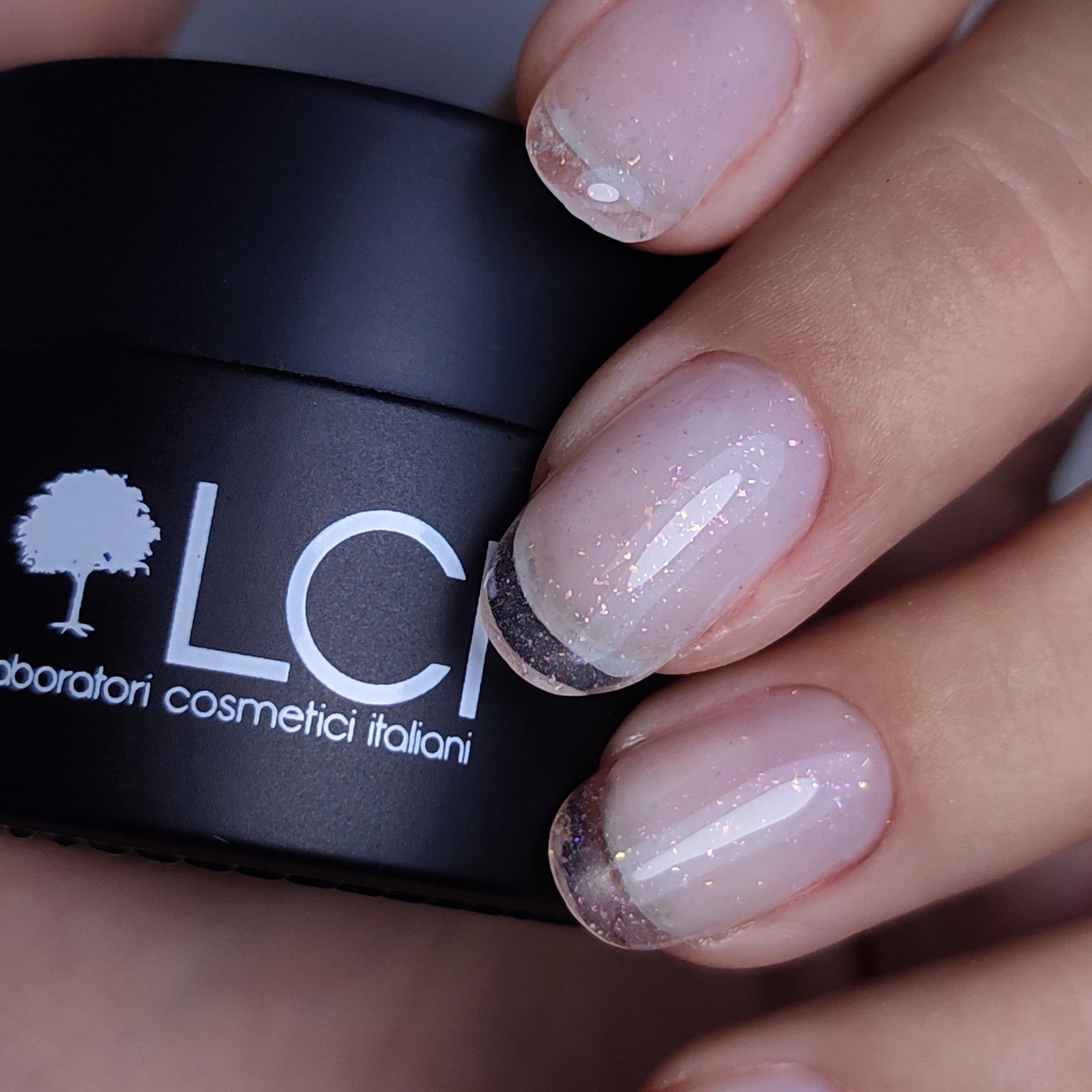Vasetto nero con logo LCI e scritta. Mano con unghie smaltate, french manicure con glitter.