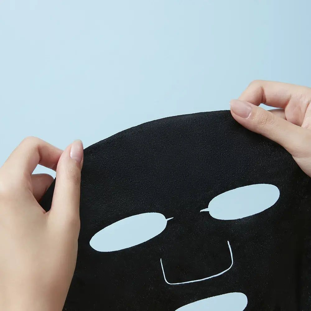 Maschera facciale nera con fori per occhi e bocca, tenuta da mani.