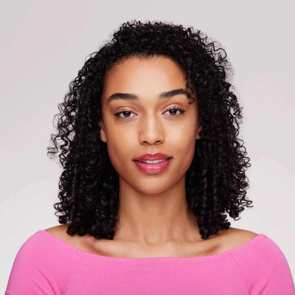Ritratto di donna con capelli ricci. Indossa rossetto rosa. Lo sfondo è grigio chiaro.