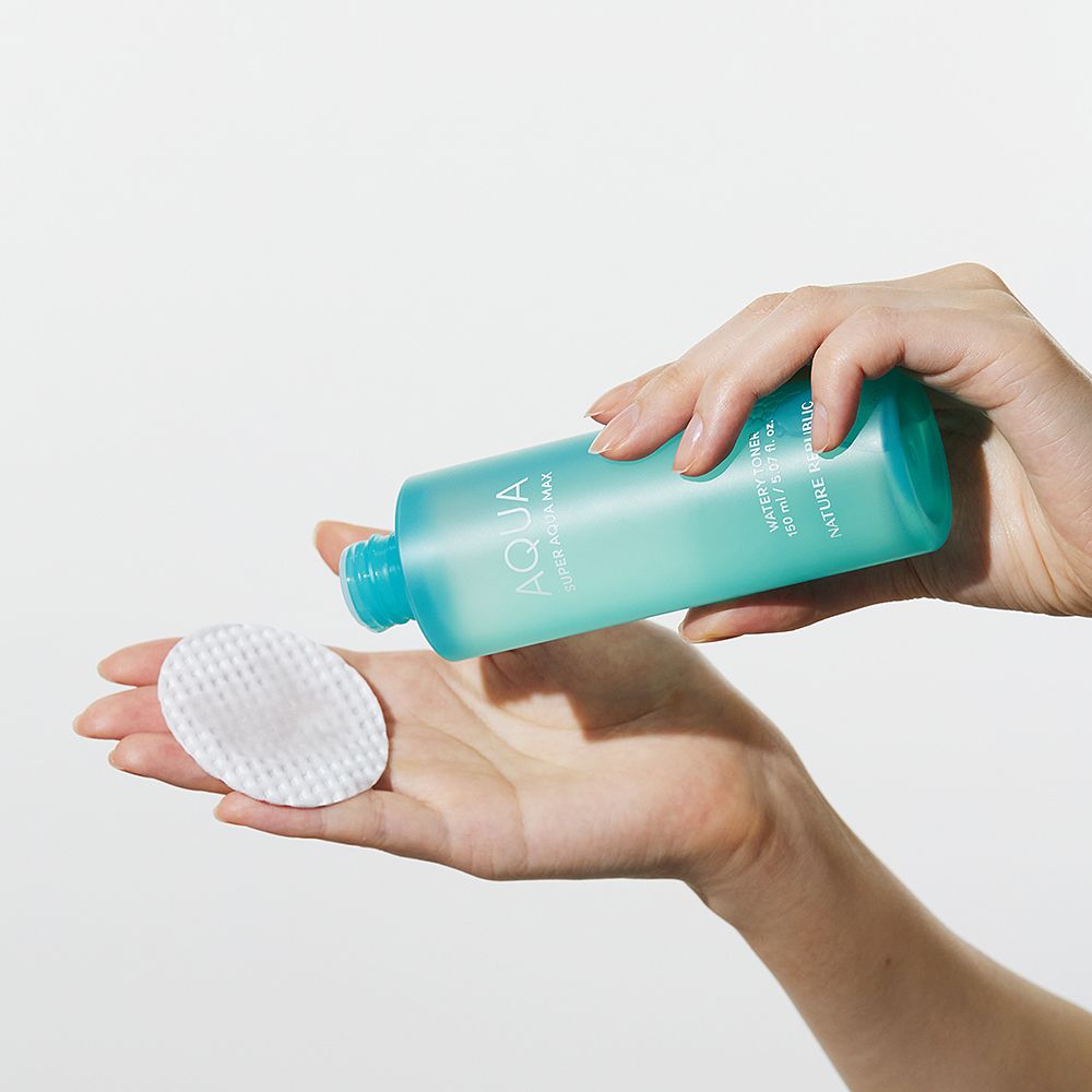 Mani che tengono una bottiglia turchese e un dischetto di cotone. Sulla bottiglia si legge "AQUA".