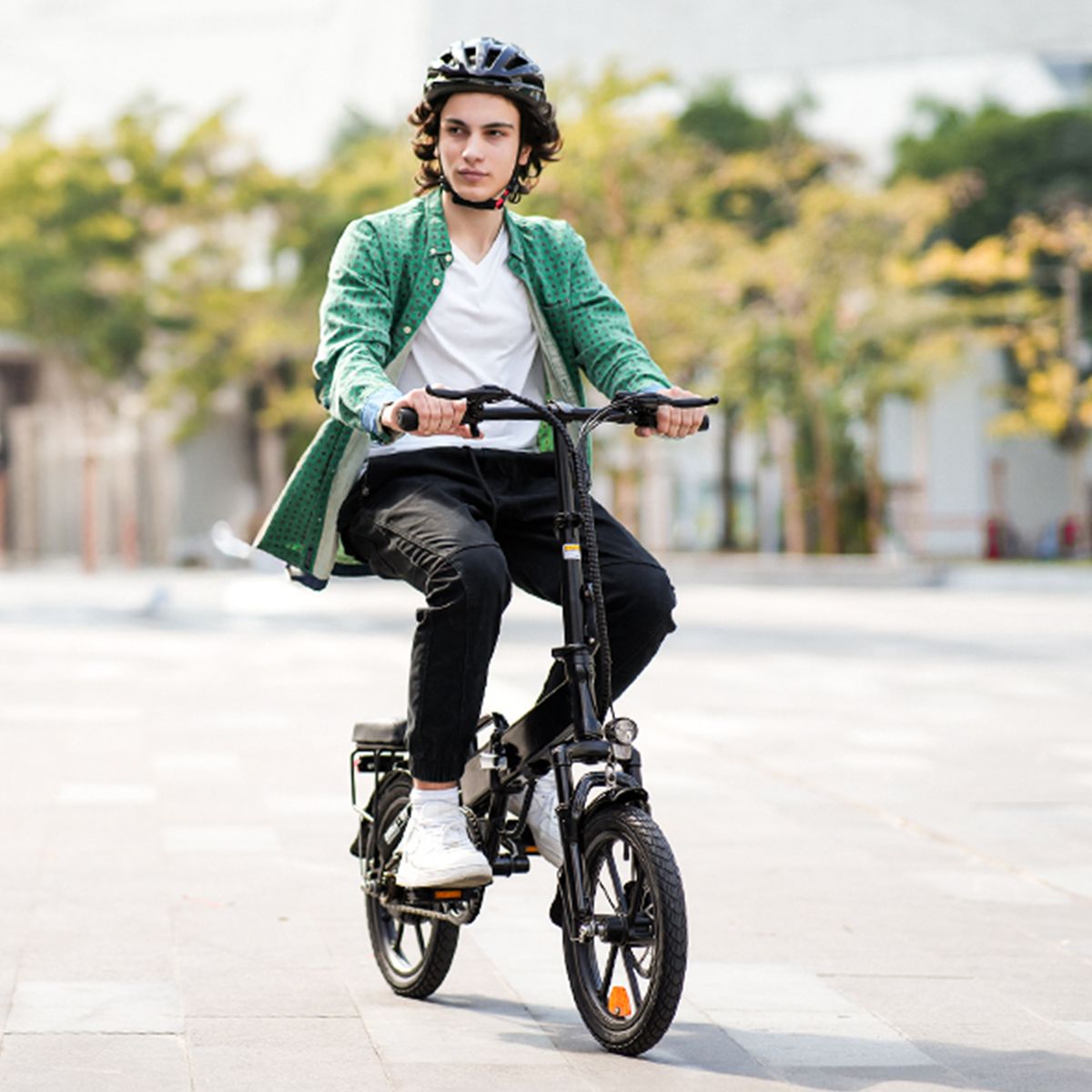 Persona in bicicletta su una bicicletta elettrica pieghevole nera. Indossa casco e giacca verde. Sfondo: alberi.